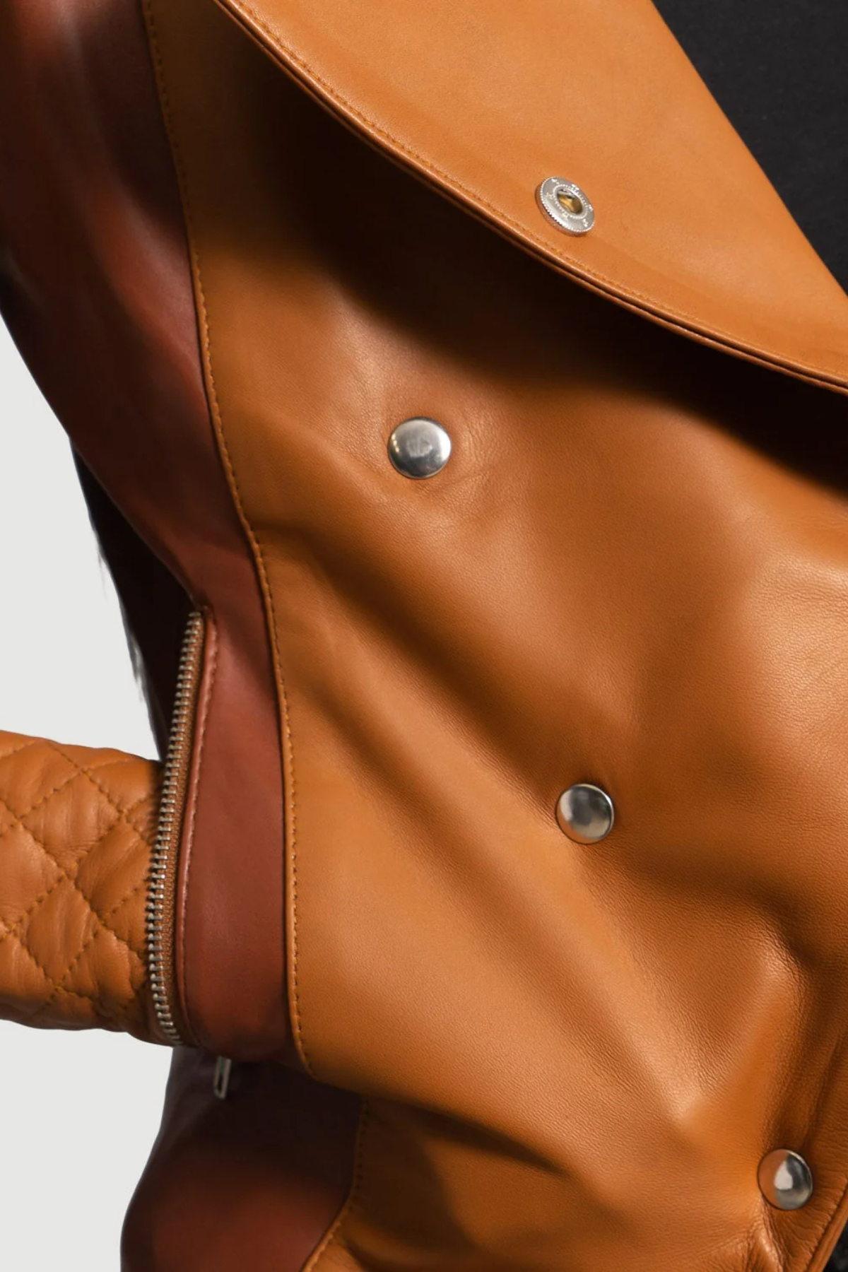 Close-up of a brown leather jacket with buttons and a zipper.